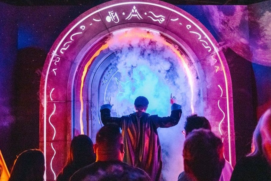 A photo of a group of people on a dark stage standing in front of a glowing arch.