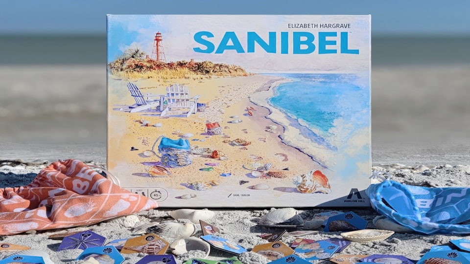 A board game box sitting on a towel on a sandy beach floor.
